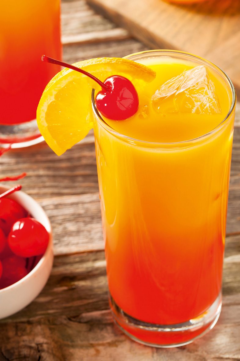 Tequila Sunrise mit einer Kirsche und Orangenscheibe auf einem dunklen Tisch